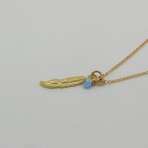 May include: A gold chain necklace with a small gold feather charm and a light blue opal bead.