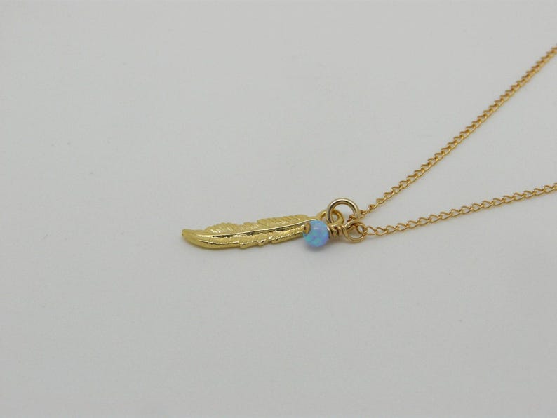 May include: A gold chain necklace with a small gold feather charm and a light blue opal bead.