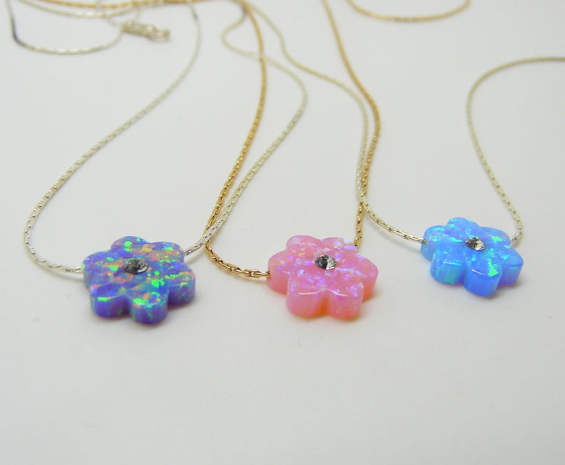 Puede incluir: Tres collares con colgantes en forma de flor. Los colgantes son de colores opalinos: morado, rosa y azul, cada uno con un peque&ntilde;o cristal en el centro. Las cadenas son delicadas, en plata y oro.