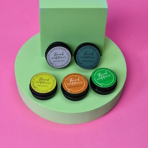 May include: Five small round containers of thread conditioner in different colours. The containers are labelled with the text "Thread conditioner" and a scent name: "Birthday Suit", "Nordic Wood", "Fresh Daisy", "Mangapple Fizz", and "Coconut Lime".