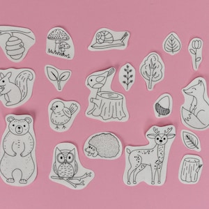 Könnte beinhalten: Ein Set mit 14 Schwarzweißillustrationen von Waldtieren und Pflanzen auf rosa Hintergrund. Die Illustrationen zeigen ein Eichhörnchen, einen Bären, eine Eule, ein Reh, einen Fuchs, einen Vogel, eine Schnecke, einen Pilz, einen Bienenstock, eine Eichel und Blätter.