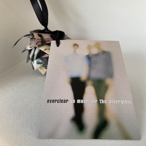 May include: A handmade ornament with a black ribbon and a tag. The ornament is made of folded paper in shades of black, white, and gray. The tag has the text "everclear so much for the afterglow".