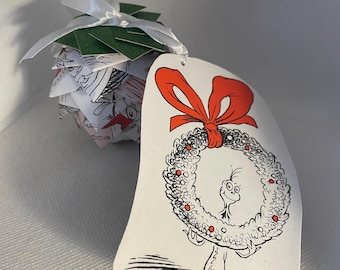 May include: A whimsical Christmas ornament featuring a Dr. Seuss-inspired design. The ornament is a layered paper sphere with a green top and a white ribbon. A tag with a red bow and a wreath with a character holding it is attached.