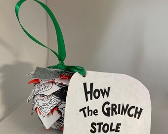 May include: A handmade Christmas ornament with a green ribbon. The ornament is made of layered paper with black and white illustrations and red accents. A white tag attached to the ornament reads "How The Grinch Stole Christmas".