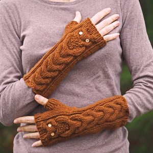 May include: A pair of brown knitted fingerless gloves with a cable knit pattern and gold buttons. The gloves are worn by a person with a brown sweater.