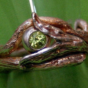 May include: A silver ring with a green gemstone set in a twisted branch design.