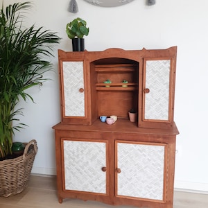Peut inclure: Un buffet en bois avec un motif en chevron blanc et gris sur les portes. Le buffet a deux portes supérieures, une étagère intermédiaire et deux portes inférieures. Le buffet est brun et a une finition vieillie.