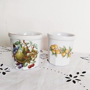 Peut inclure: Deux tasses en céramique blanche avec des motifs floraux. Une tasse présente une poire, des raisins et des cerises, tandis que l'autre présente une branche de fruits jaunes.