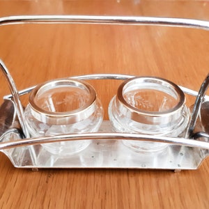May include: Silver serving tray with two clear glass jars with etched designs. The tray has a handle and is designed to hold two small jars.