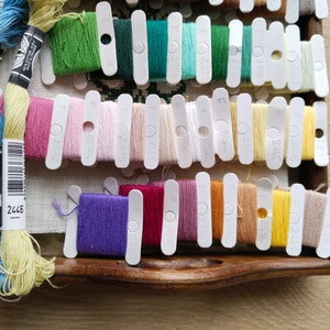 May include: A close-up of a wooden box filled with colorful embroidery floss spools. The spools are organized by color and labeled with DMC numbers. The box is open and the spools are visible. The DMC number 2445 is visible on the box.