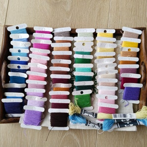 May include: A wooden tray filled with rows of colorful embroidery floss spools. The floss is organized by color and is ready for use in a craft project.