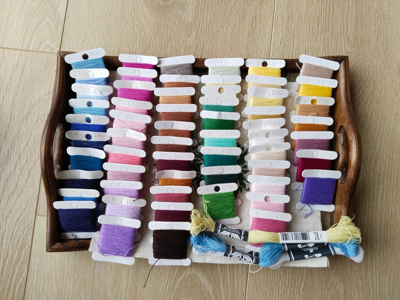 May include: A wooden tray filled with rows of colorful embroidery floss spools. The floss is organized by color and is ready for use in a craft project.