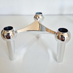 Peut inclure: Un bougeoir argenté avec trois bougeoirs sphériques. Le bougeoir a un design triangulaire avec trois pieds cylindriques. La surface réfléchissante du bougeoir crée un aspect moderne et élégant.