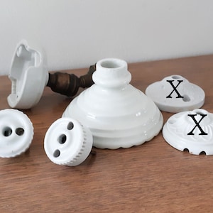 Pode incluir: Uma coleção de componentes elétricos de porcelana branca, incluindo tomadas, um castiçal e suportes de teto. Os componentes estão dispostos sobre uma superfície de madeira, mostrando seu design vintage e detalhes intrincados.