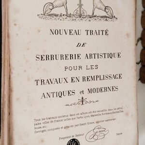 May include: Antique book cover with French text and illustrations. The cover features two greyhound-like dogs flanking a decorative key design. The title reads "NOUVEAU TRAITÉ DE SERRURERIE ARTISTIQUE".