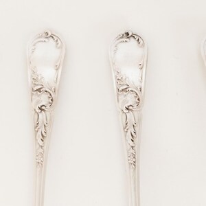 May include: Six silver spoons with intricate floral and scrollwork patterns. The spoons are displayed in a row against a white backdrop. The spoons have a classic, elegant appearance, suitable for formal dining or display.