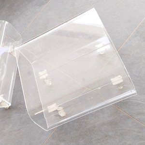 May include: Clear acrylic display boxes with hinged lids and silver-toned hardware. The boxes are angled and designed to showcase items. The transparent material allows for full visibility of the contents, making them suitable for retail or personal display.