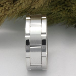 Puede incluir: Un anillo de plata con acabado cepillado y un diseño único entrelazado. El anillo está hecho de múltiples bandas que encajan entre sí para crear un aspecto texturizado.