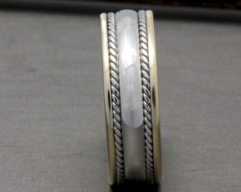 May include: A silver and gold wedding band with a rope design. The band is wide and has a rounded profile.