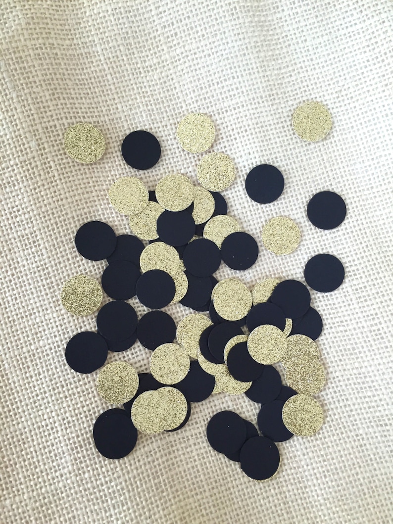 Puede incluir: Una colecci&oacute;n de c&iacute;rculos de confeti negros y dorados. Los c&iacute;rculos est&aacute;n esparcidos sobre una superficie de arpillera beige.