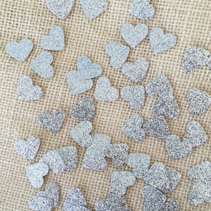 Puede incluir: Una superficie de arpillera est&aacute; cubierta con corazones de purpurina plateada. Los corazones est&aacute;n dispersos aleatoriamente por la superficie.