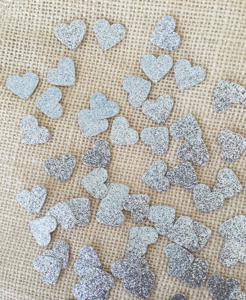 Puede incluir: Una superficie de arpillera est&aacute; cubierta con corazones de purpurina plateada. Los corazones est&aacute;n dispersos aleatoriamente por la superficie.
