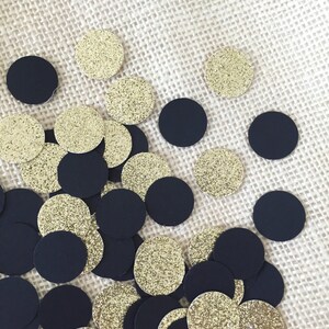 Puede incluir: Una colecci&oacute;n de c&iacute;rculos de confeti negros y dorados. El confeti est&aacute; esparcido sobre una superficie de arpillera beige.