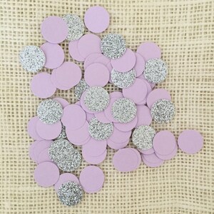 May include: A collection of purple and silver confetti circles. The confetti is scattered on a burlap surface.