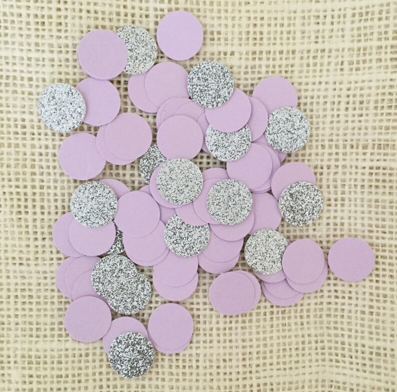 May include: A collection of purple and silver confetti circles. The confetti is scattered on a burlap surface.
