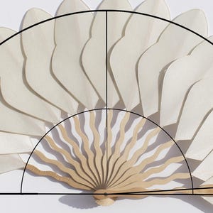 Può includere: Un ventaglio bianco aperto con manico in legno. Il design del ventaglio presenta una serie di forme curve a forma di petalo. Il ventaglio è parzialmente aperto, rivelando gli intricati dettagli della sua costruzione. Il ventaglio è largo circa 30 cm.