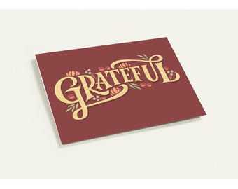 Könnte beinhalten: Rechteckige Karte mit dem Wort "GRATEFUL" in goldener Schrift. Verziert mit kleinen Kürbissen und floralen Akzenten. Der Hintergrund ist ein tiefes Burgunderrot, vor einem weißen Hintergrund. Für Herbst oder Erntedank.