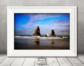 May include: A framed photograph of two large rock formations on a beach with a blue sky and white clouds. The rocks are reflected in the water.