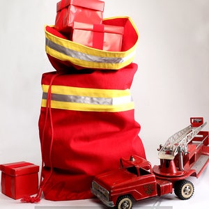 May include: A red canvas bag with yellow and silver reflective stripes, filled with red wrapped gifts. A red toy fire truck with a ladder is in the foreground.