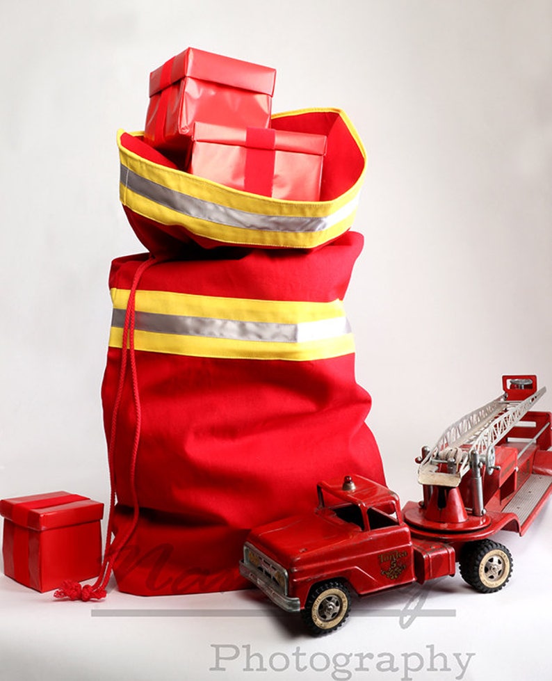 May include: A red canvas bag with yellow and silver reflective stripes, filled with red wrapped gifts. A red toy fire truck with a ladder is in the foreground.