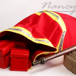 May include: A red fire hose bag with yellow reflective tape, partially open to reveal red gift boxes. A brown fire hose with a brass nozzle is lying on the ground next to the bag.