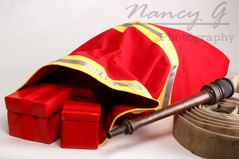 May include: A red fire hose bag with yellow reflective tape, partially open to reveal red gift boxes. A brown fire hose with a brass nozzle is lying on the ground next to the bag.
