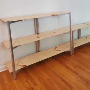 May include: Two wooden shelves with silver metal frames. The shelves are empty and are sitting on a wooden floor.