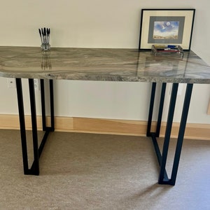 May include: A long, curved, light brown granite countertop with black metal legs. The countertop has a unique, organic shape and a polished finish.