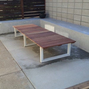 May include: A long, rectangular wooden table with a white metal frame. The table is sitting on a concrete patio.