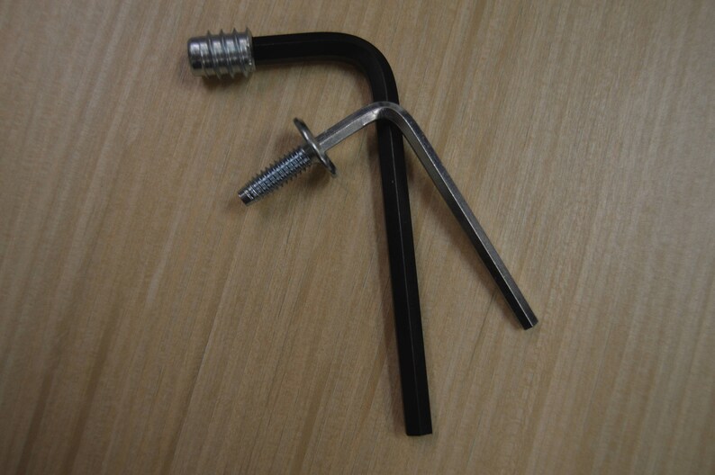 May include: A black L-shaped wrench with a silver screw and a silver metal piece attached to the wrench.