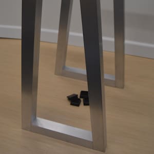 Op de afbeelding: Set zilveren metalen tafelpoten met een rechthoekig frame-ontwerp. De schuine poten zien er stevig uit. Kleine zwarte plastic voetjes liggen op de vloer. De tafelpoten zijn ontworpen voor meubelconstructie.
