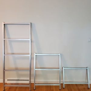 May include: Three silver metal bookshelves of varying sizes. The largest bookshelf has four shelves, the middle bookshelf has three shelves, and the smallest bookshelf has two shelves.