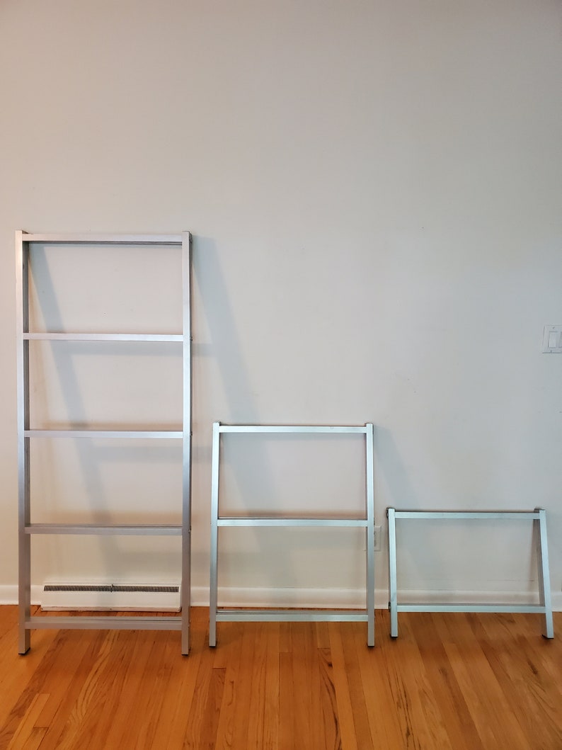 May include: Three silver metal bookshelves of varying sizes. The largest bookshelf has four shelves, the middle bookshelf has three shelves, and the smallest bookshelf has two shelves.