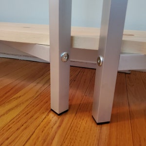May include: Close-up of two silver metal legs with black plastic feet. The legs are attached to a wooden shelf.