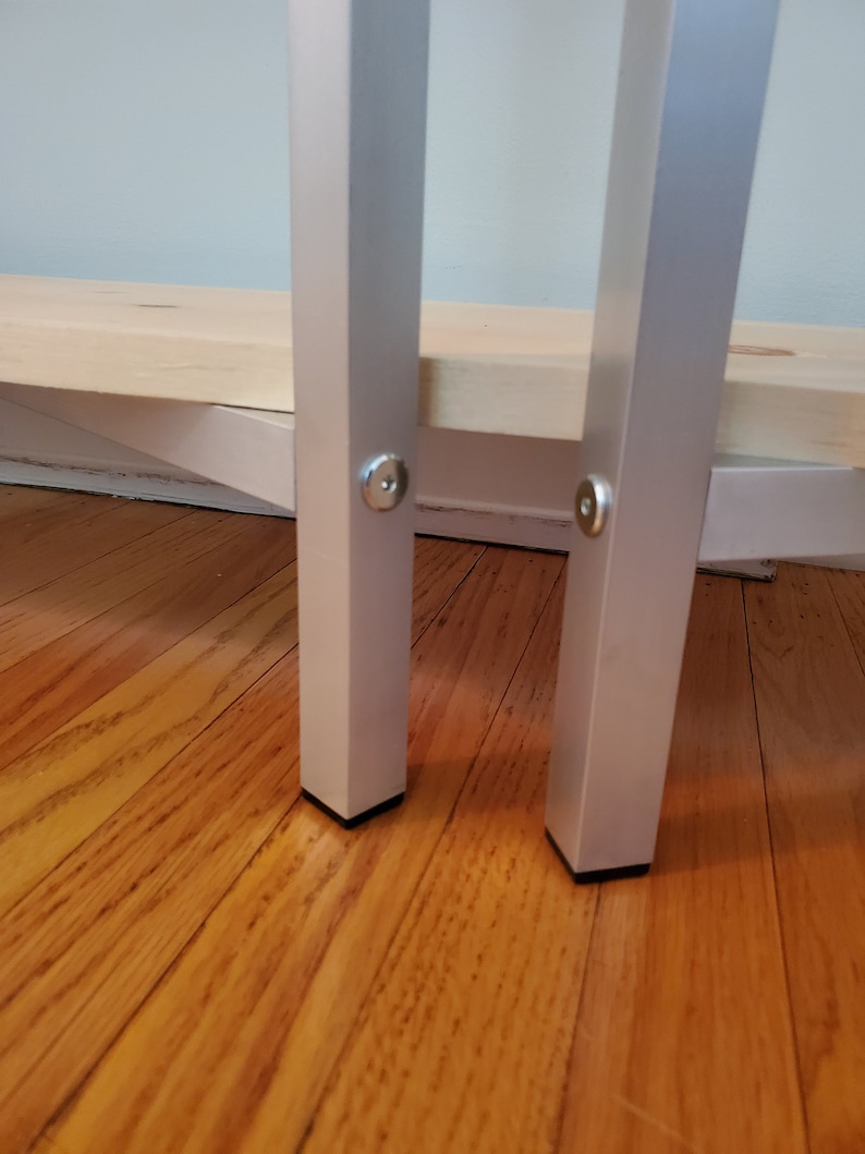 May include: Close-up of two silver metal legs with black plastic feet. The legs are attached to a wooden shelf.