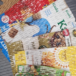 May include: Close-up of several cereal boxes, including Kashi brand, with a variety of flavors like Island Vanilla, Pumpkin, and Simple Mills. The boxes are torn and ripped, showing the cereal inside.
