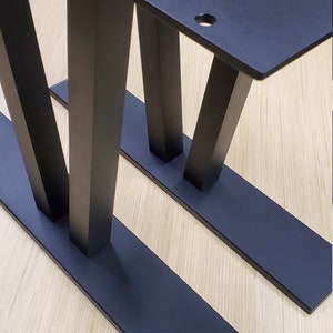 May include: Two black metal table legs with a V-shaped design and a rectangular base.