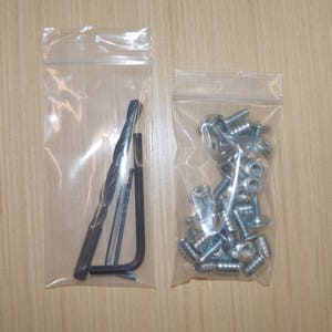 May include: Two clear plastic bags containing hardware. One bag contains a drill bit and a small wrench. The other bag contains a pile of silver screws.