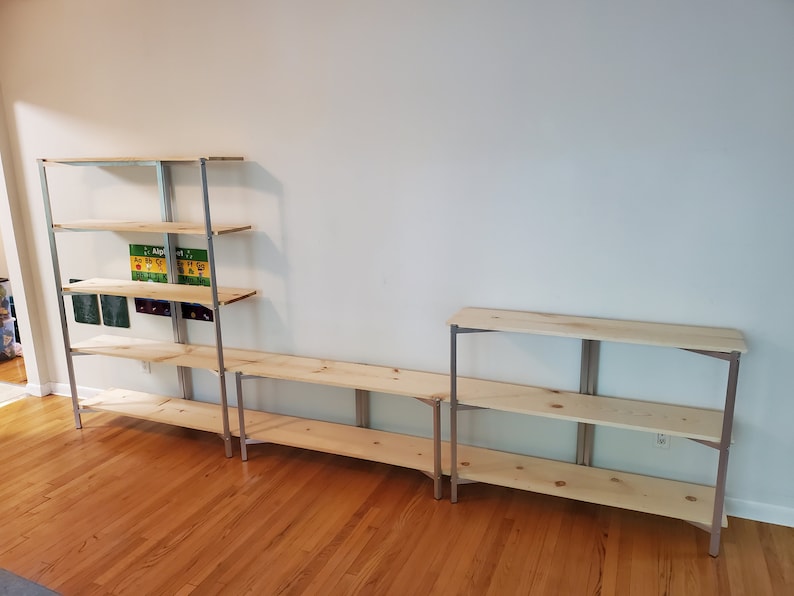 May include: Three metal shelving units with wooden shelves. The shelves are empty. The shelves are against a white wall.