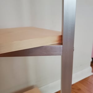 May include: A wooden shelf with a silver metal frame. The shelf is made of light wood and the frame is made of a brushed silver metal.